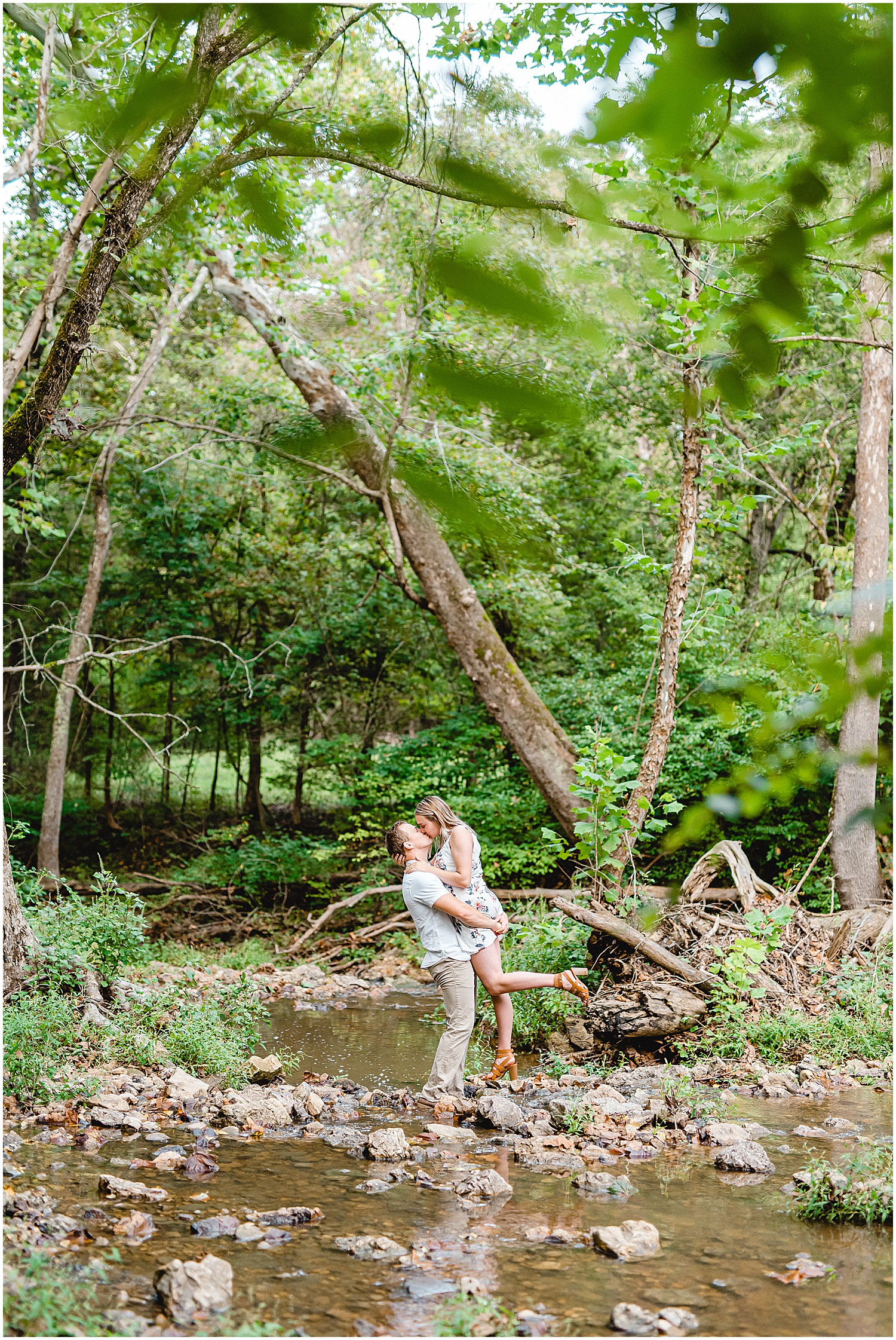 couple kisses standing on rocks in creek bed during engagement session in missouri