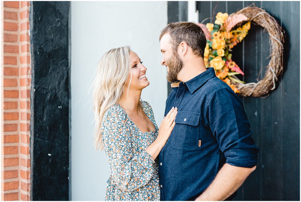 couple smiles at each other in front of church doors during engagement session