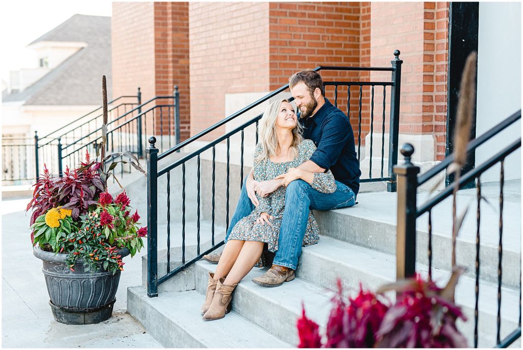 couple sits on stairs in front of church doors and smiles during missouri engagement session