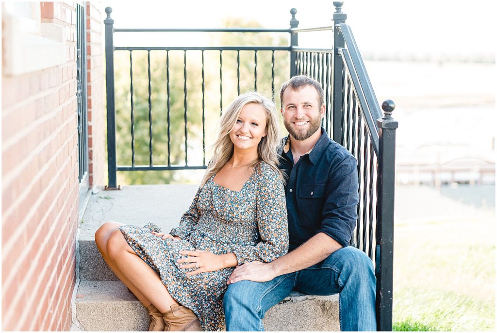 couple sits on stairs and smiles at camera for engagement session at church