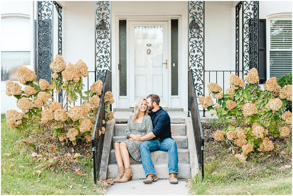 couple sits on stairs of white church house during fall engagement session in missouri