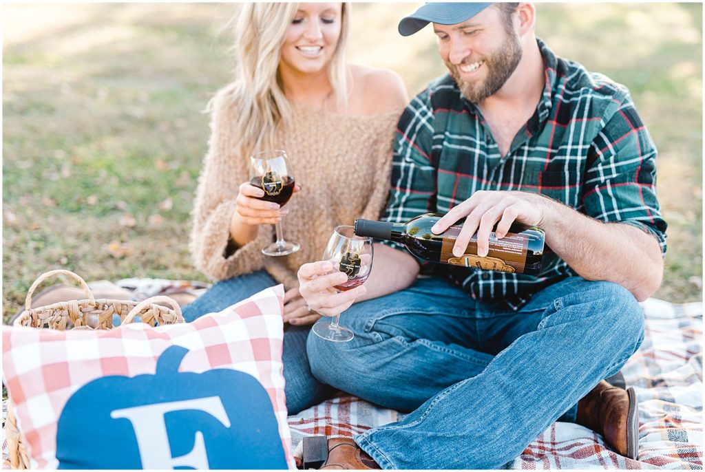 man pours local wine during picnic engagement session on missouri farm