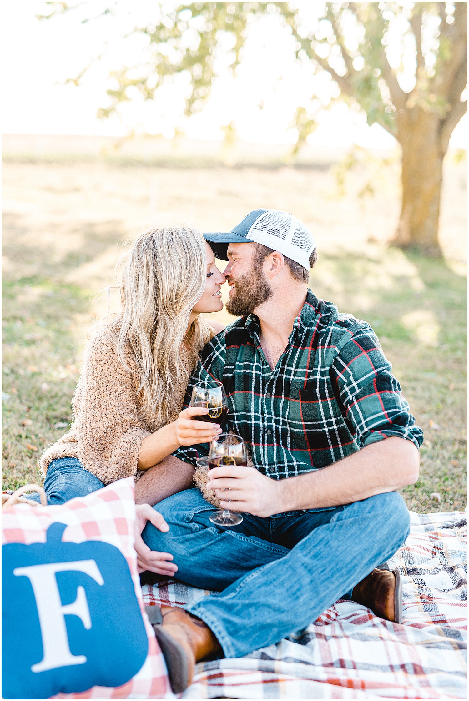 couple kisses while drinking wine on picnic blanket for missouri farm engagement session
