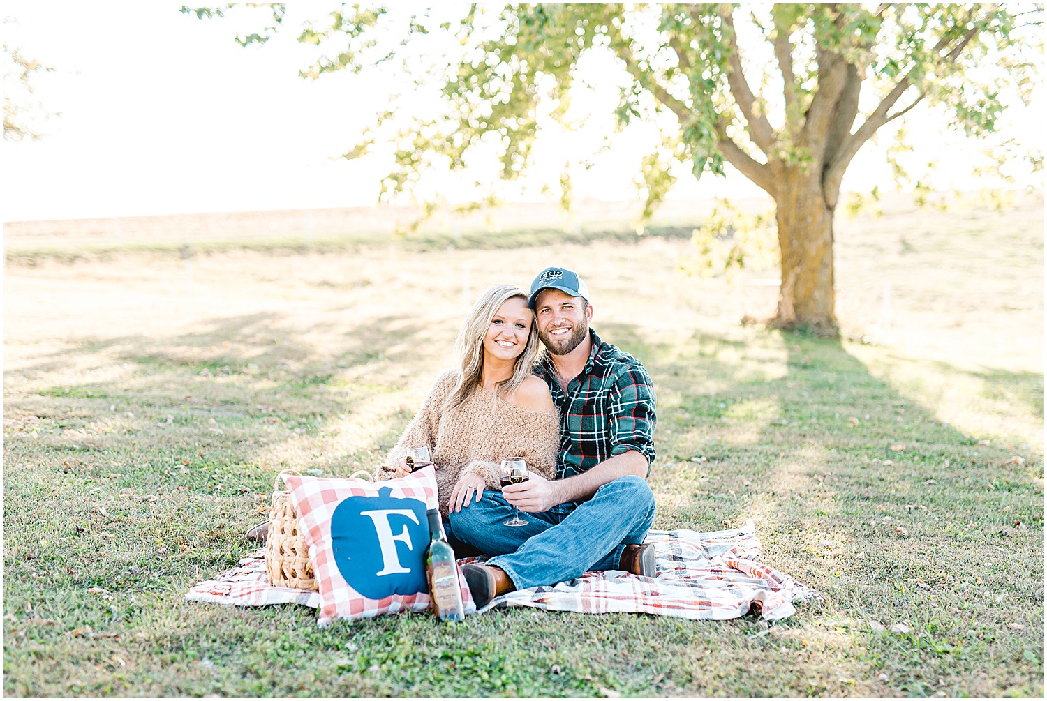 engaged couple sits on picnic blanket under tree for engagement session