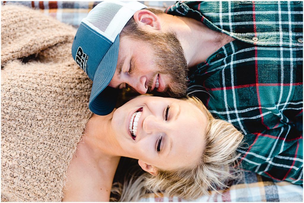 couple lays on blanket and laughs during engagement pictures