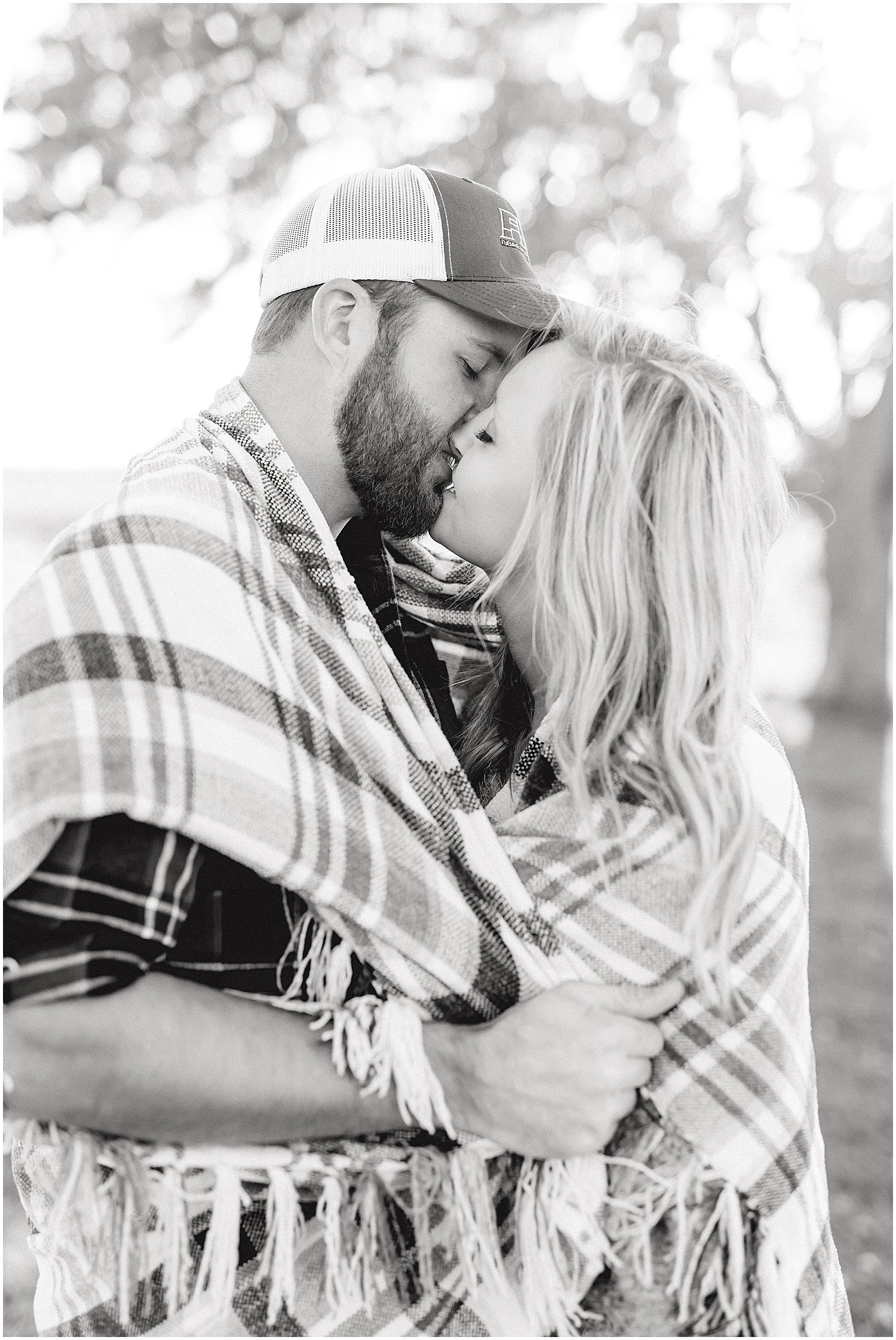 black and white image of couple kissing wrapped in plaid blanket for engagement session on missouri farm