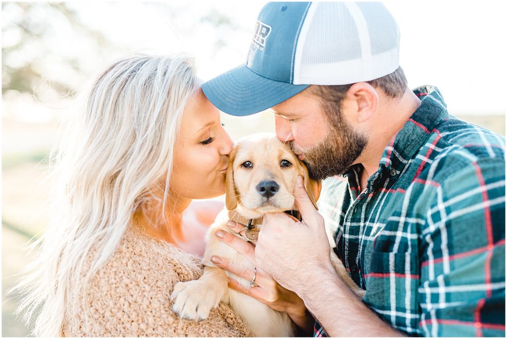 couple kisses yellow lab puppy during engagement session on missouri farm
