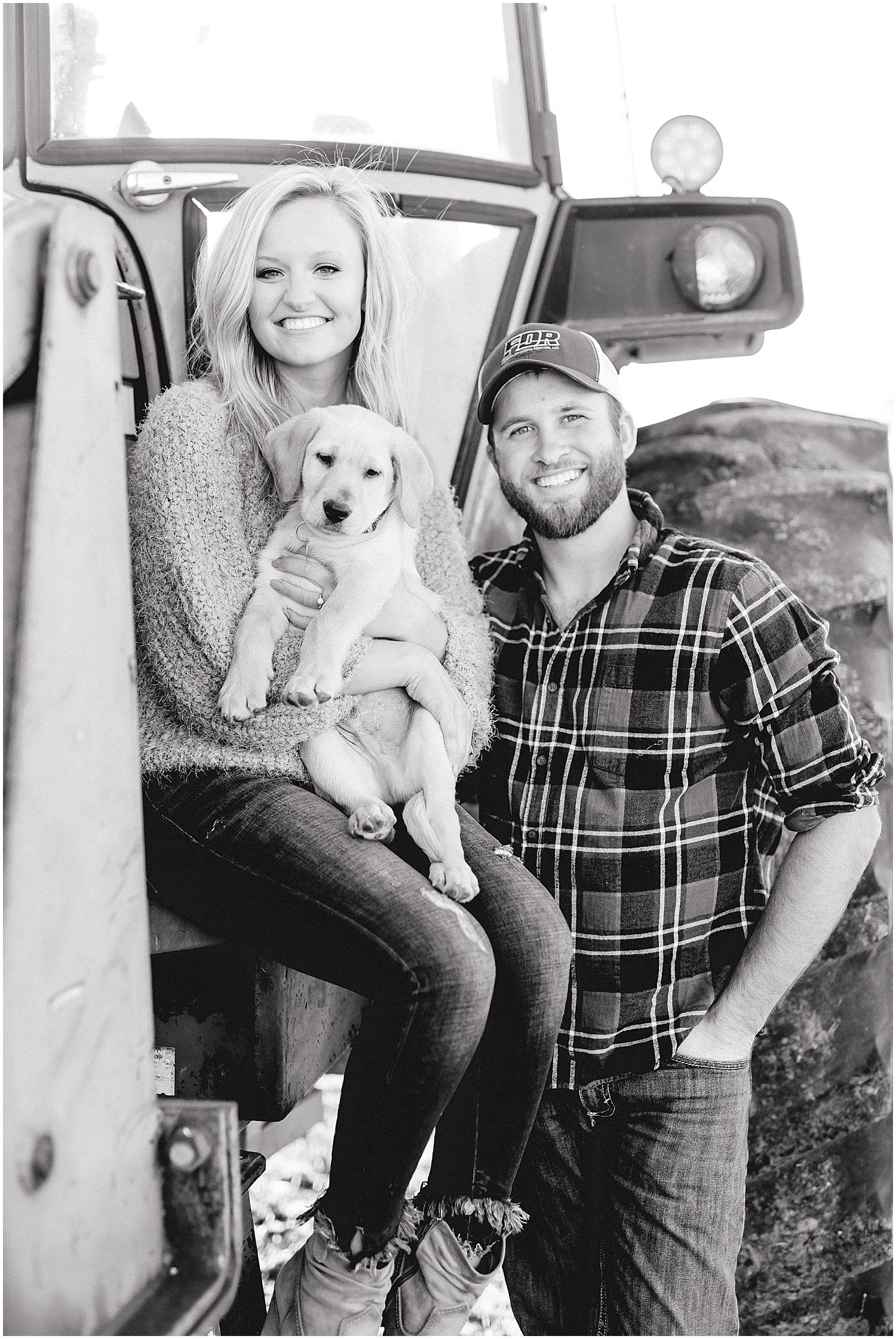 black and white image of couple holding lab puppy on tractor for pictures