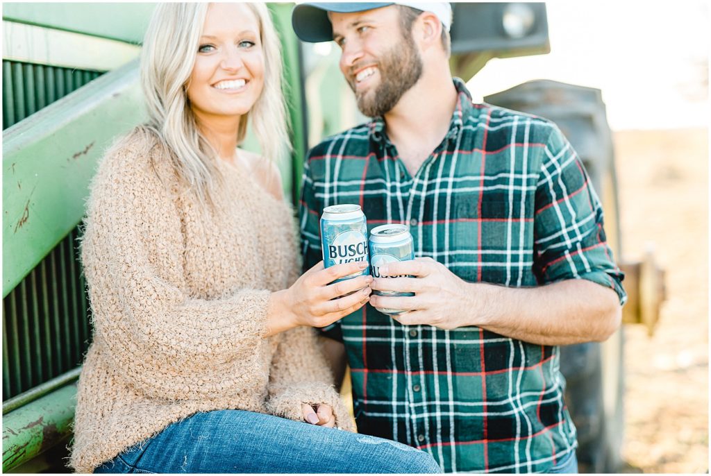 couple drinks beer while sitting on tractor during engagement session