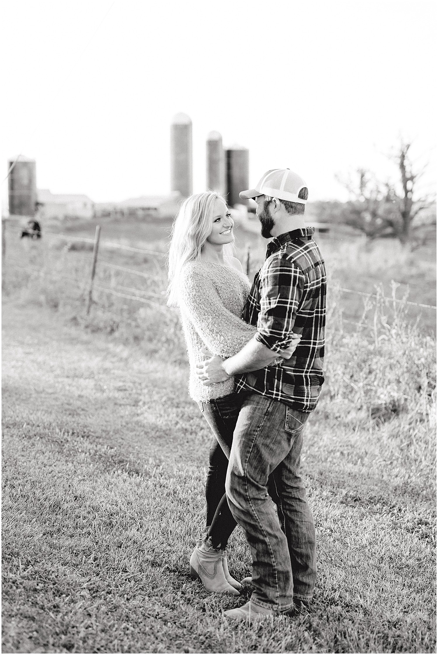 black and white image of couple hugging on grass with silos in the background during engagement session