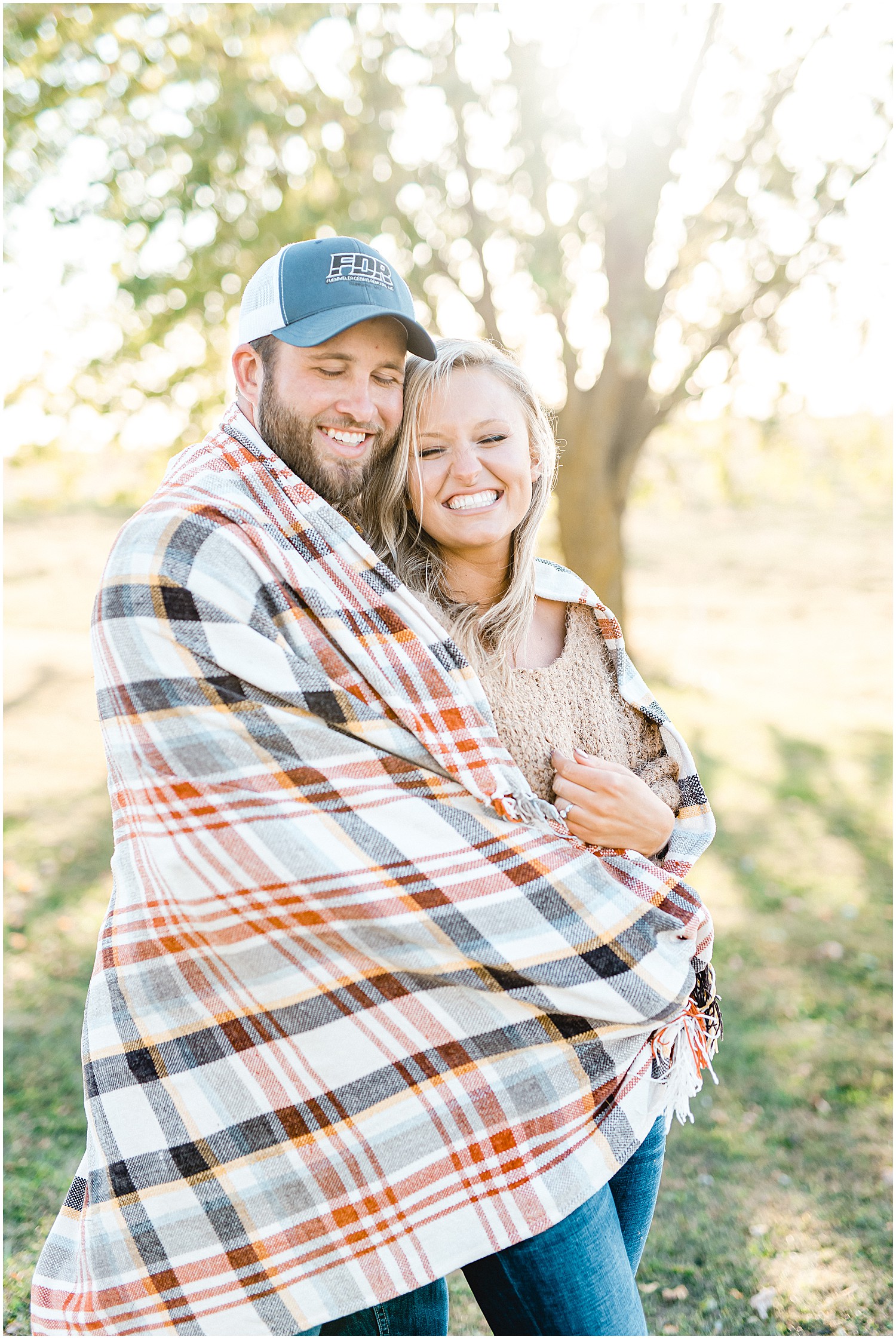 couple smiles together wrapped in blanket during engagement session