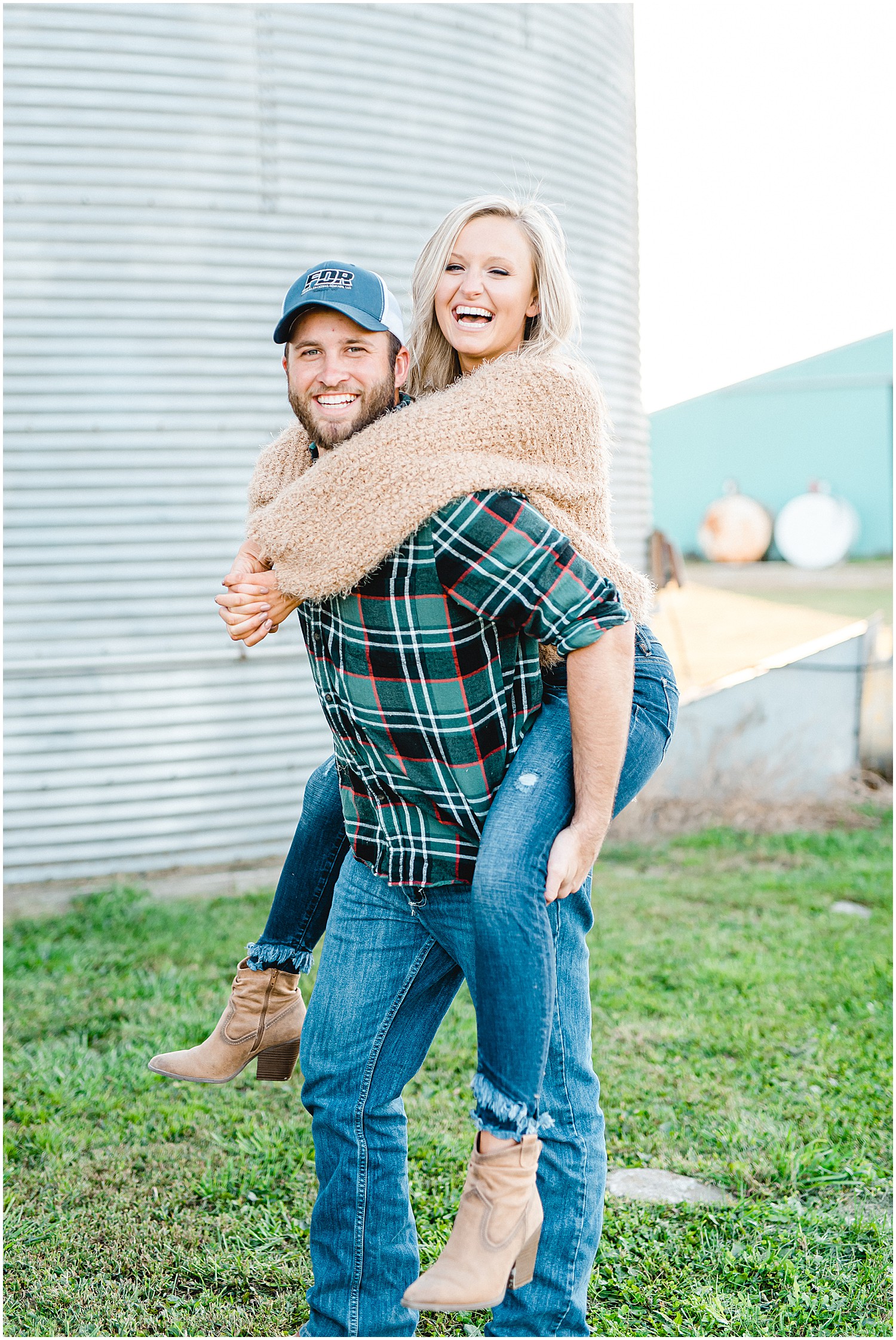 couple laughs while giving a piggy back ride in front of silo during Missouri engagement session