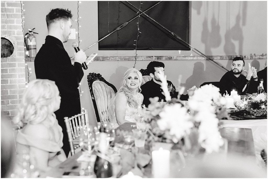 black and white image of bride crying while brother gives a toast during wedding reception