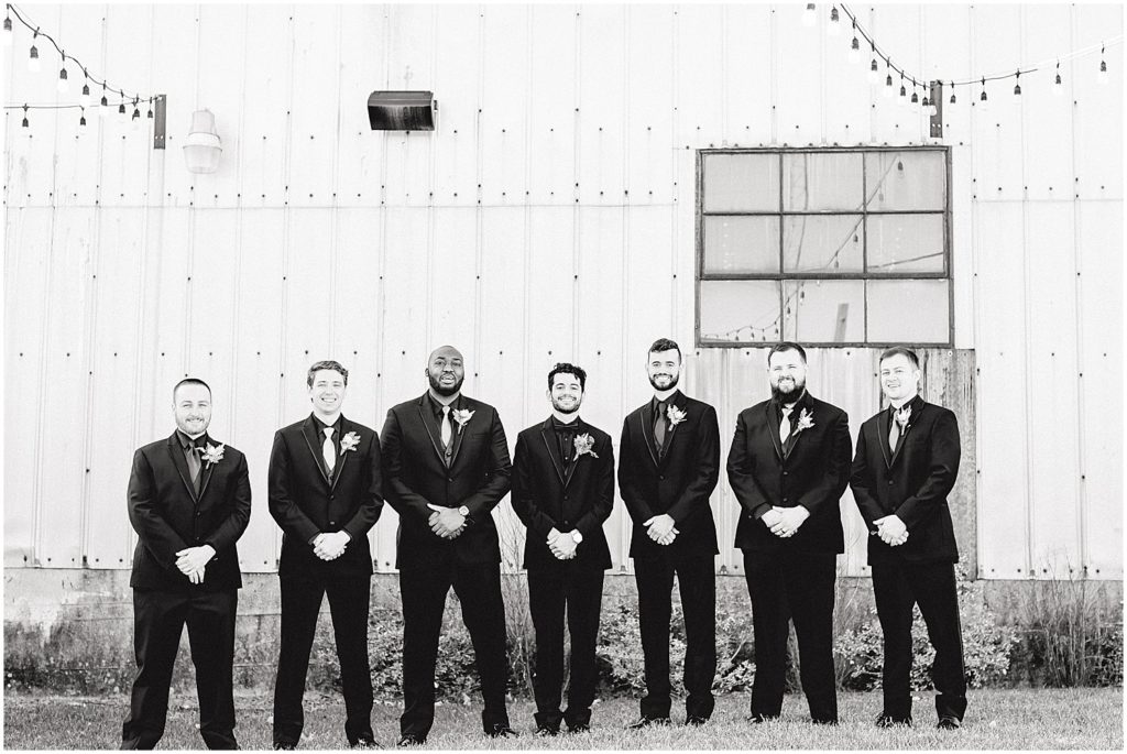 black and white image of groom and groomsmen standing outside of wedding venue