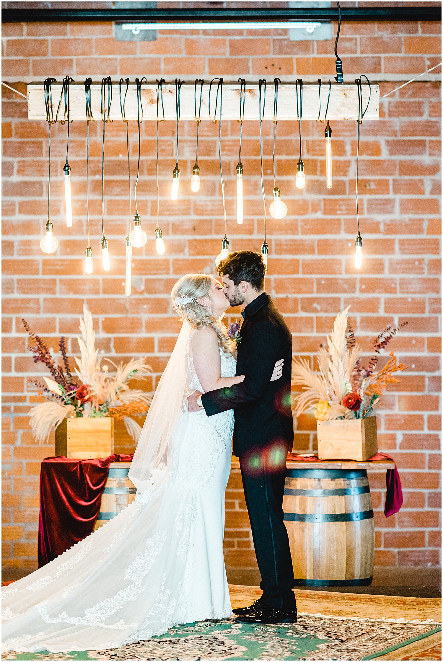 bride and groom kiss during wedding ceremony featuring fall floral decorations and rugs