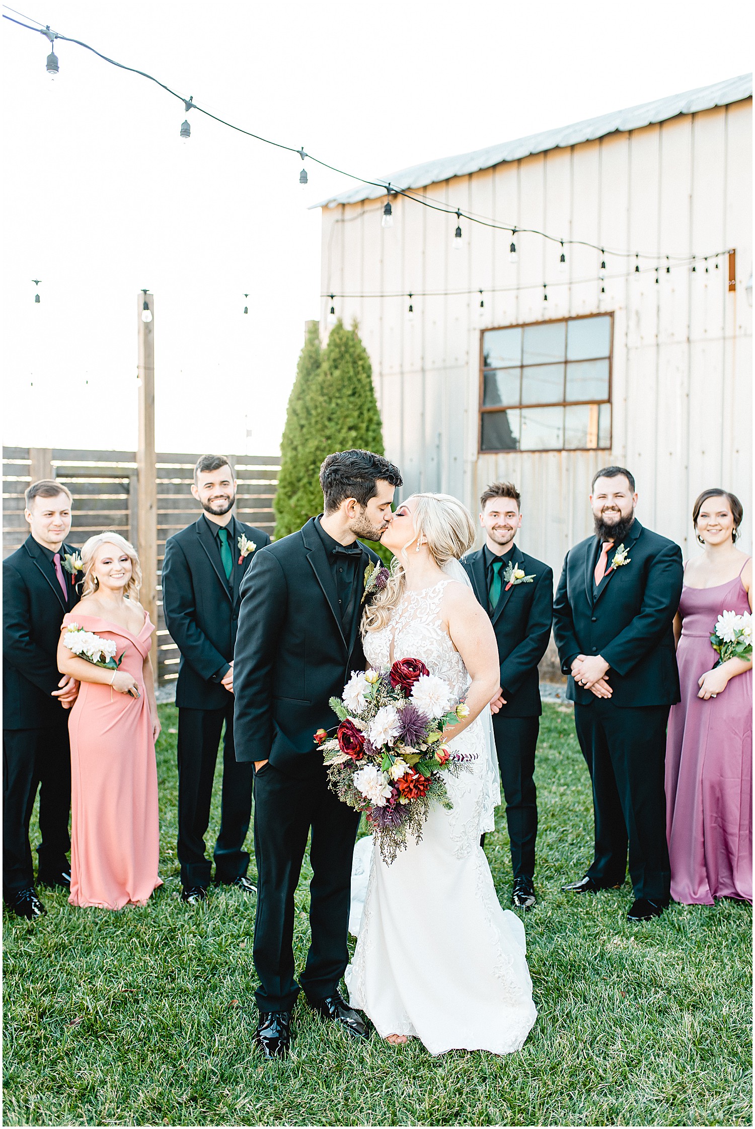 bride and groom kiss with wedding party in background