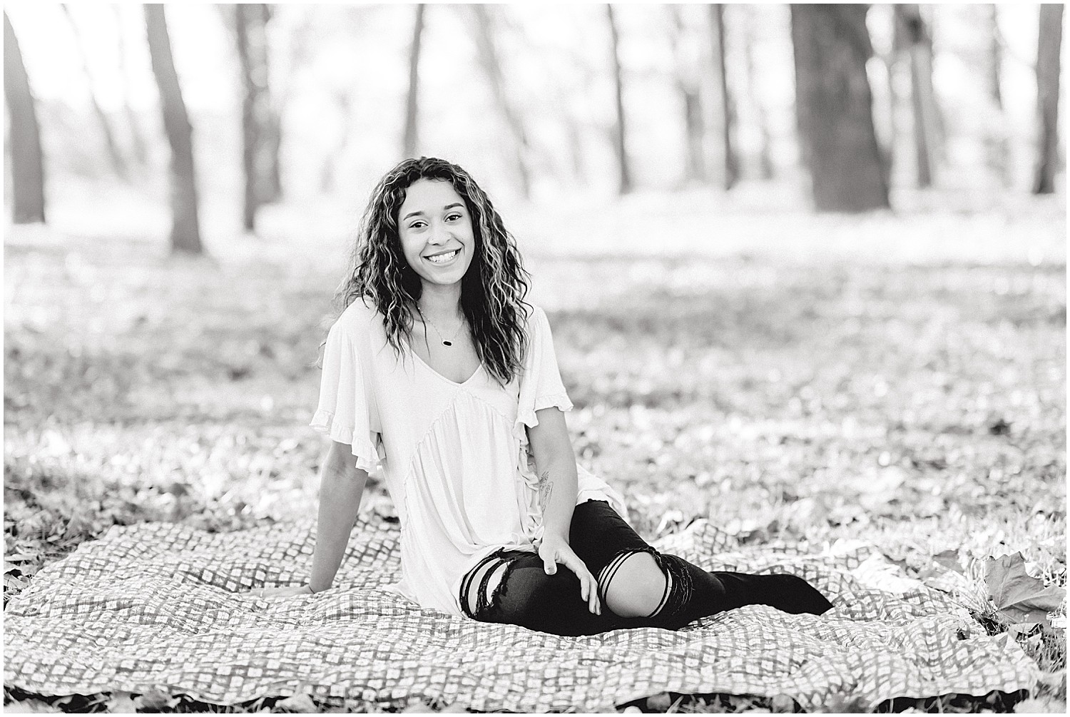 black and white image of senior girl sitting on blanket in the grass in the fall at a park