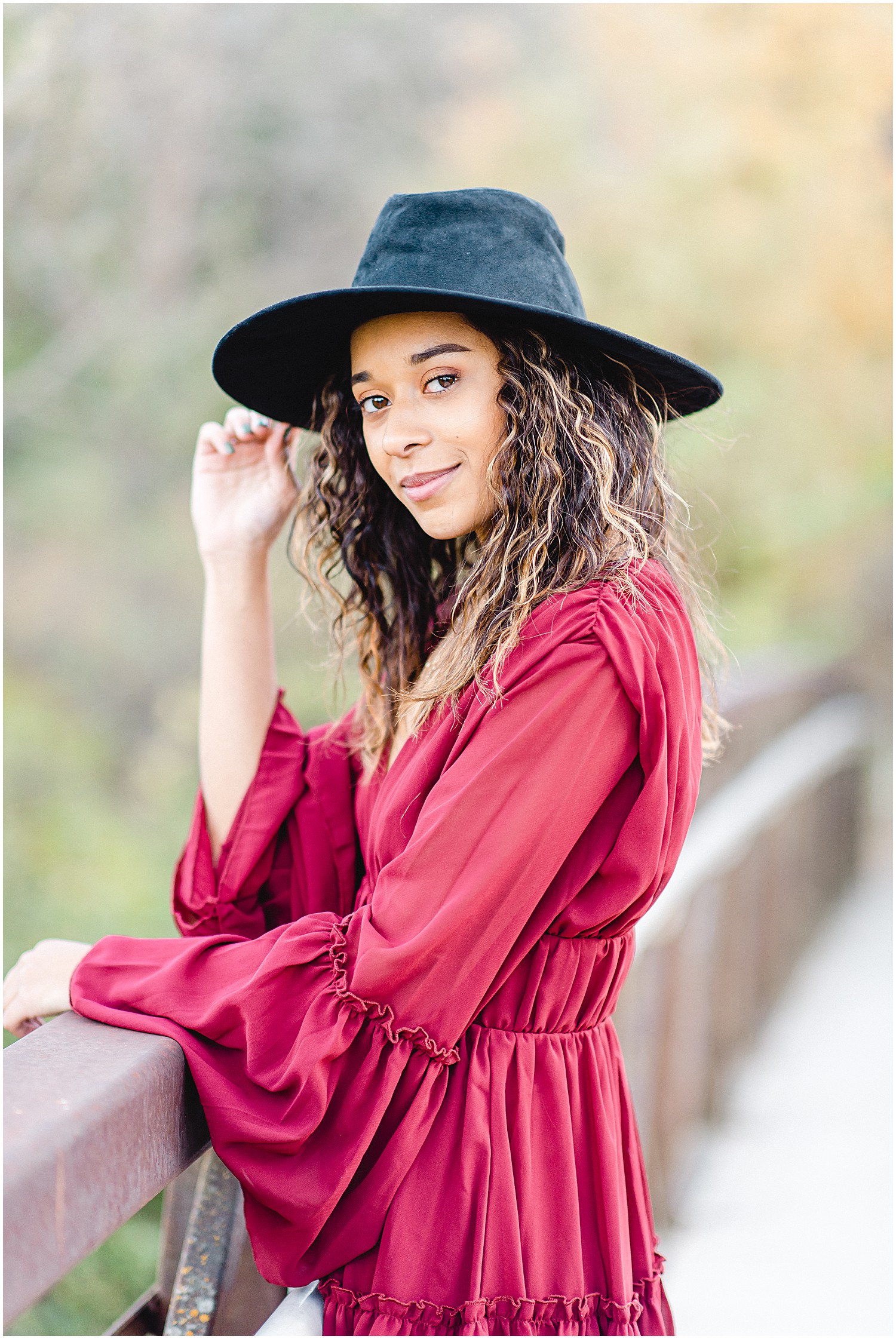 senior girl holds brim of large black hat while looking at camera during senior photos on bridge in Jefferson City, MO
