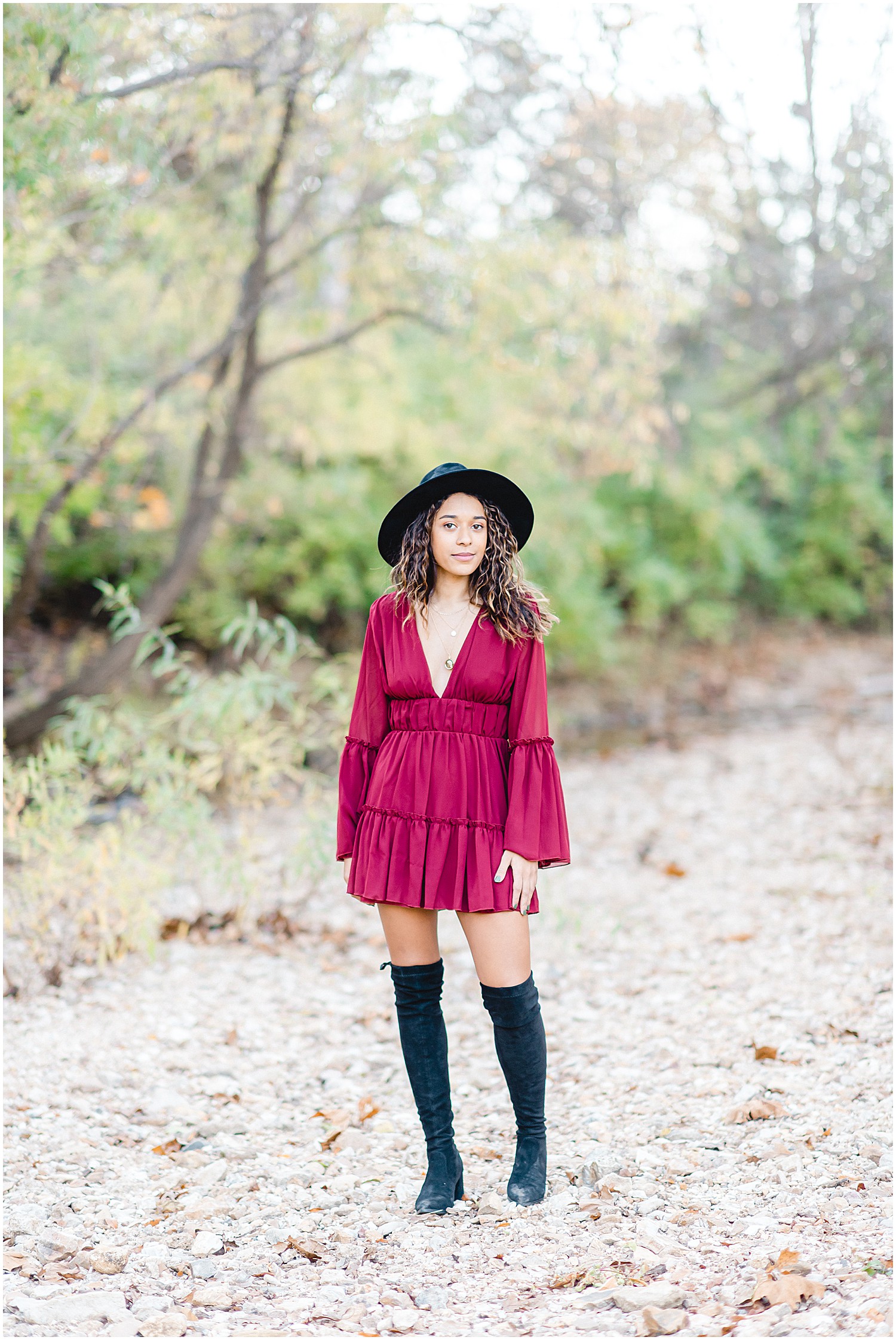 senior girl wearing large black hat and maroon mini dress and tall black boots while posing in creek bed during senior photos in Jefferson City, MO