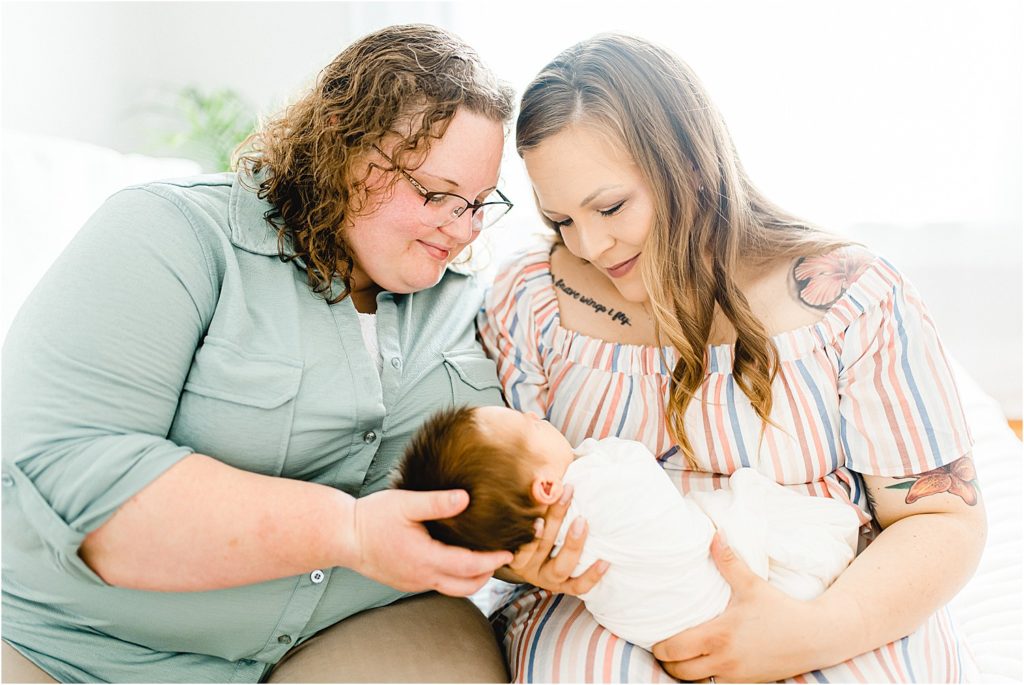 two moms hold baby boy on bed