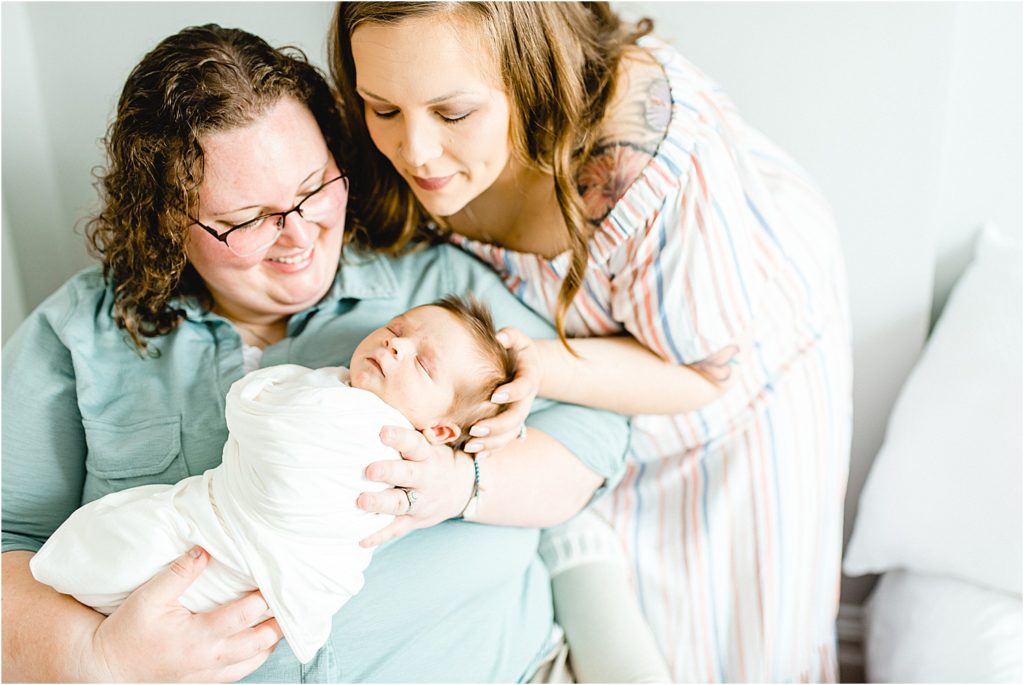 moms hold baby boy in chair for studio newborn session