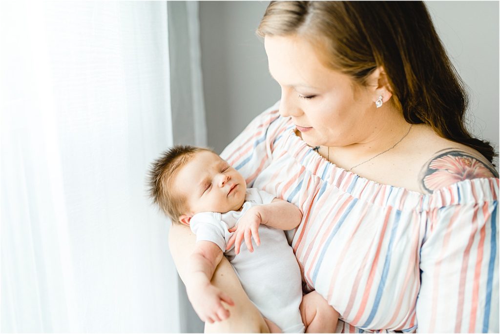 mom holds baby boy in front of window for studio newborn session