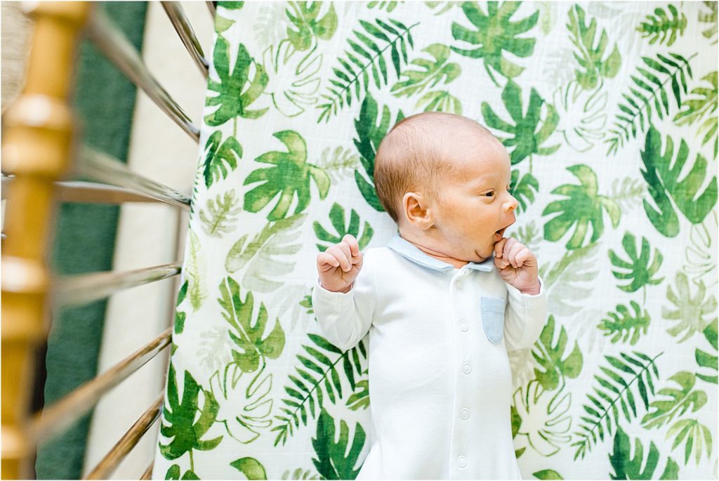 newborn baby lays on crib sheet with green leaves