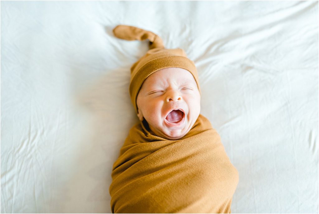 baby in gold swaddle yawns on white backdrop
