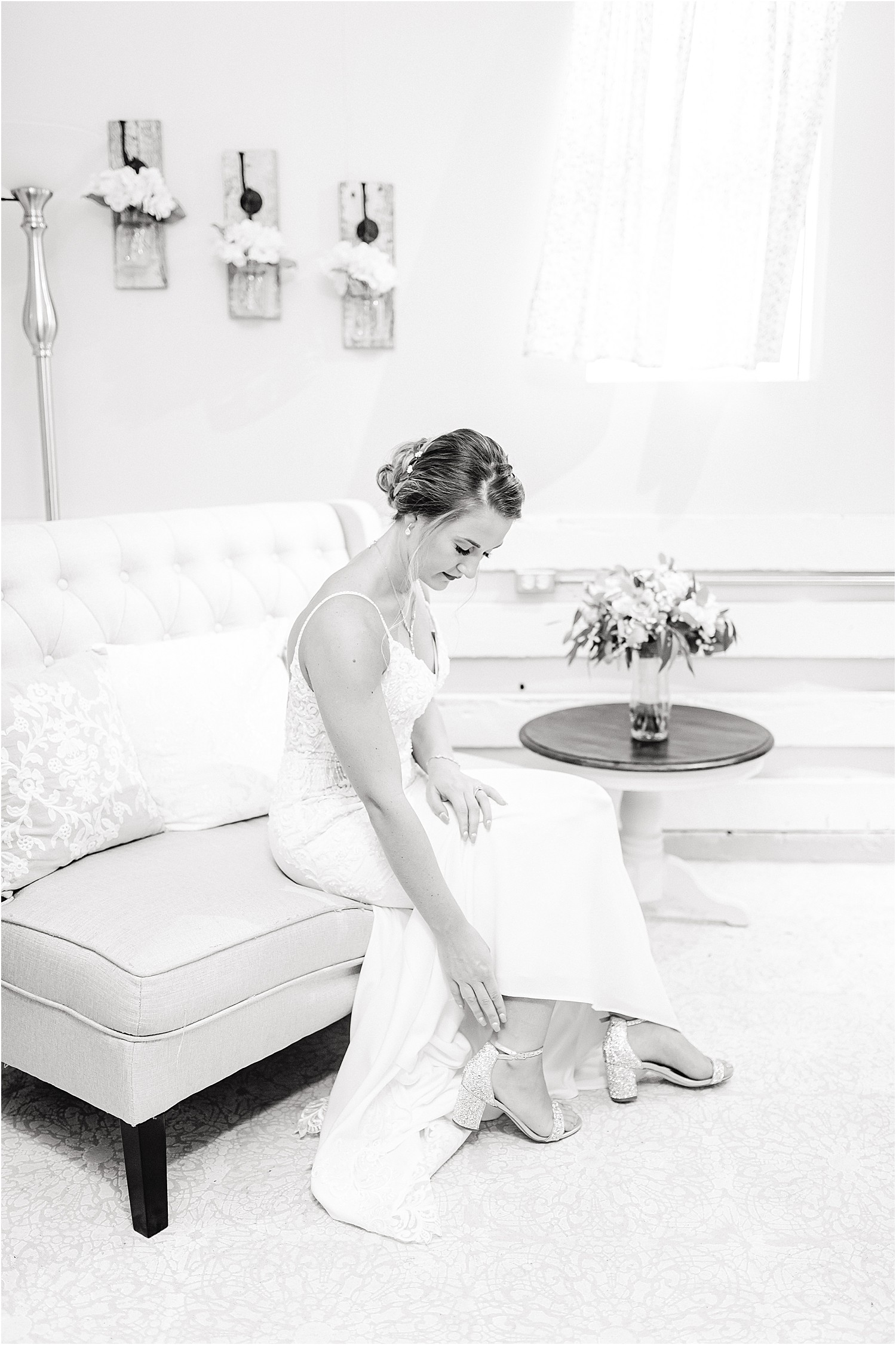 black and white image of bride putting on wedding shoes on couch