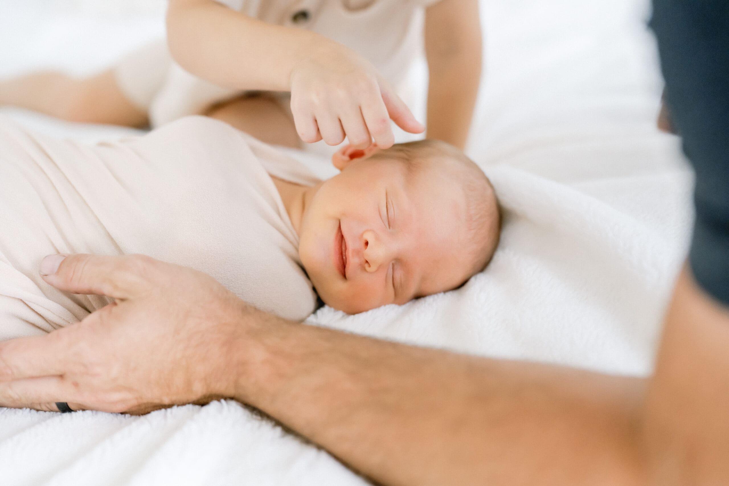 A newborn baby smiles as his brother strokes his cheek